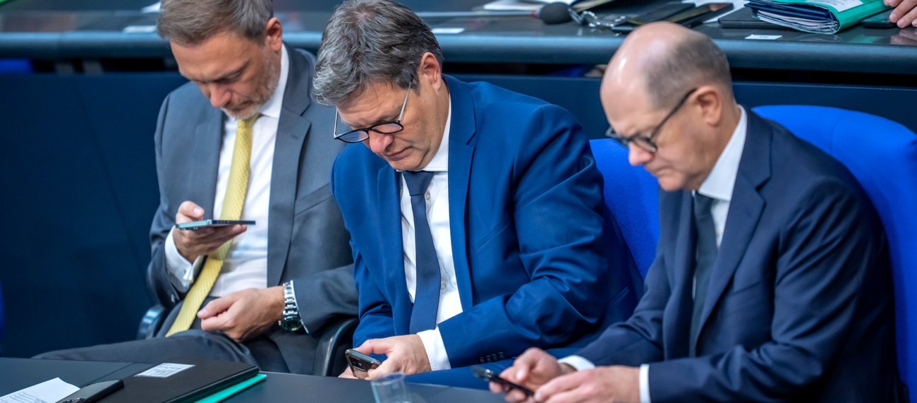 Bundeskanzler Olaf Scholz, Bundeswirtschaftsminister Robert Habeck und Bundesfinanzminister Christian Lindner sitzen auf der Regierungsbank im Plenarsaal des Bundestages und blicken auf ihre Handys © picture alliance/dpa|Michael Kappeler