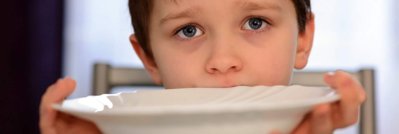 Ein Junge hält einen Teller vor seinen Mund © iStockphoto/djedzura Ein Junge hält einen Teller vor seinen Mund © iStockphoto/djedzura