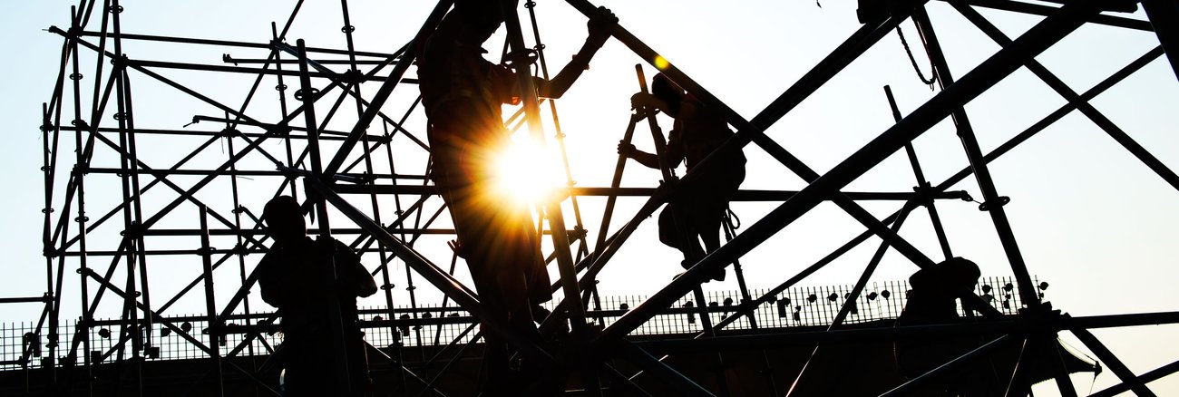 Silhouetten von Bauarbeitern, die auf einer Baustelle Gerüste montieren © iStockphoto.com/hxdbzxy