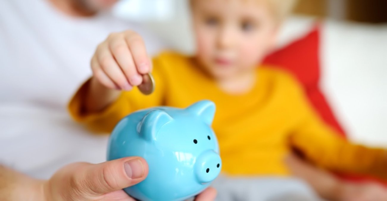 Junge mit gelbem Pullover steckt Euro-Münze in ein hellblaues Sparschwein © iStock/Finanzwissen Junge mit gelbem Pullover steckt Euro-Münze in ein hellblaues Sparschwein © iStock/Finanzwissen