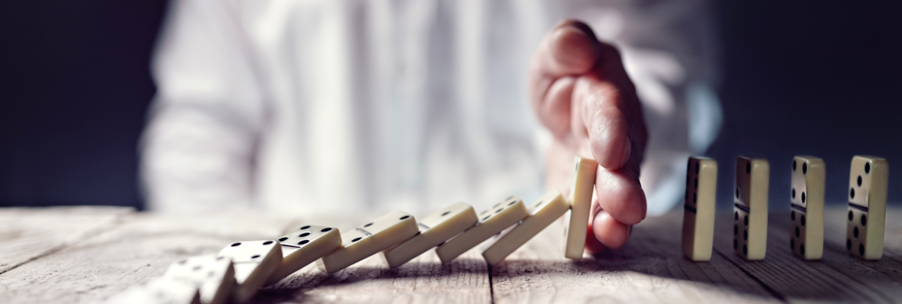 Ein Mann stoppt mit seiner Hand das Umfallen einer Domino-Kette © iStockphoto.com/BrianAJackson Ein Mann stoppt mit seiner Hand das Umfallen einer Domino-Kette © iStockphoto.com/BrianAJackson