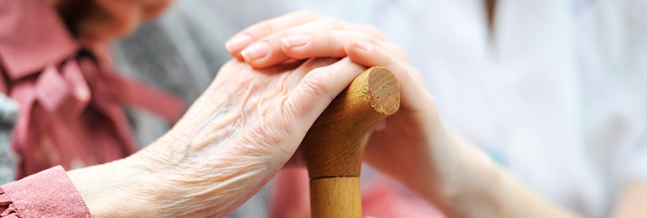 Hand einer Frau auf der Hand einer älteren Frau mit einem Gehstock Hand einer Frau auf der Hand einer älteren Frau mit einem Gehstock