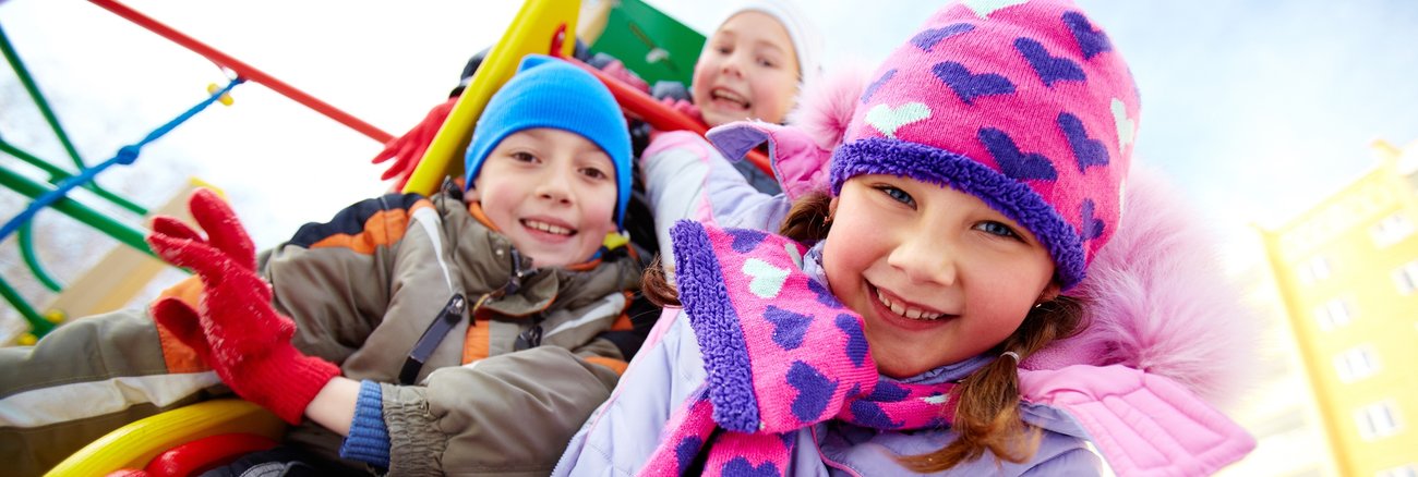 Drei Kinder im Winter auf einem Spielplatz © iStock/shironosov