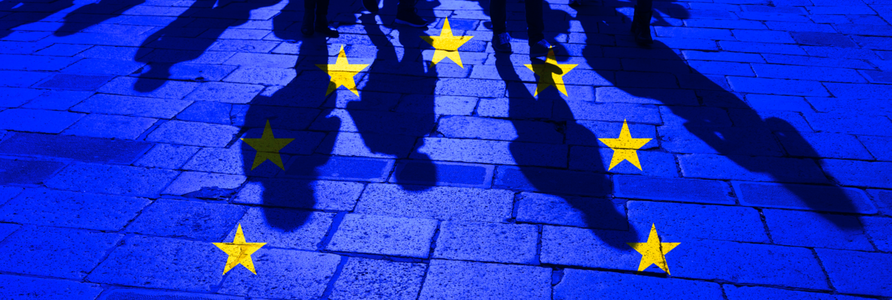 EU-Flagge über Menschenschatten Pflastersteinen © iStock/robertiez EU-Flagge über Menschenschatten Pflastersteinen © iStock/robertiez