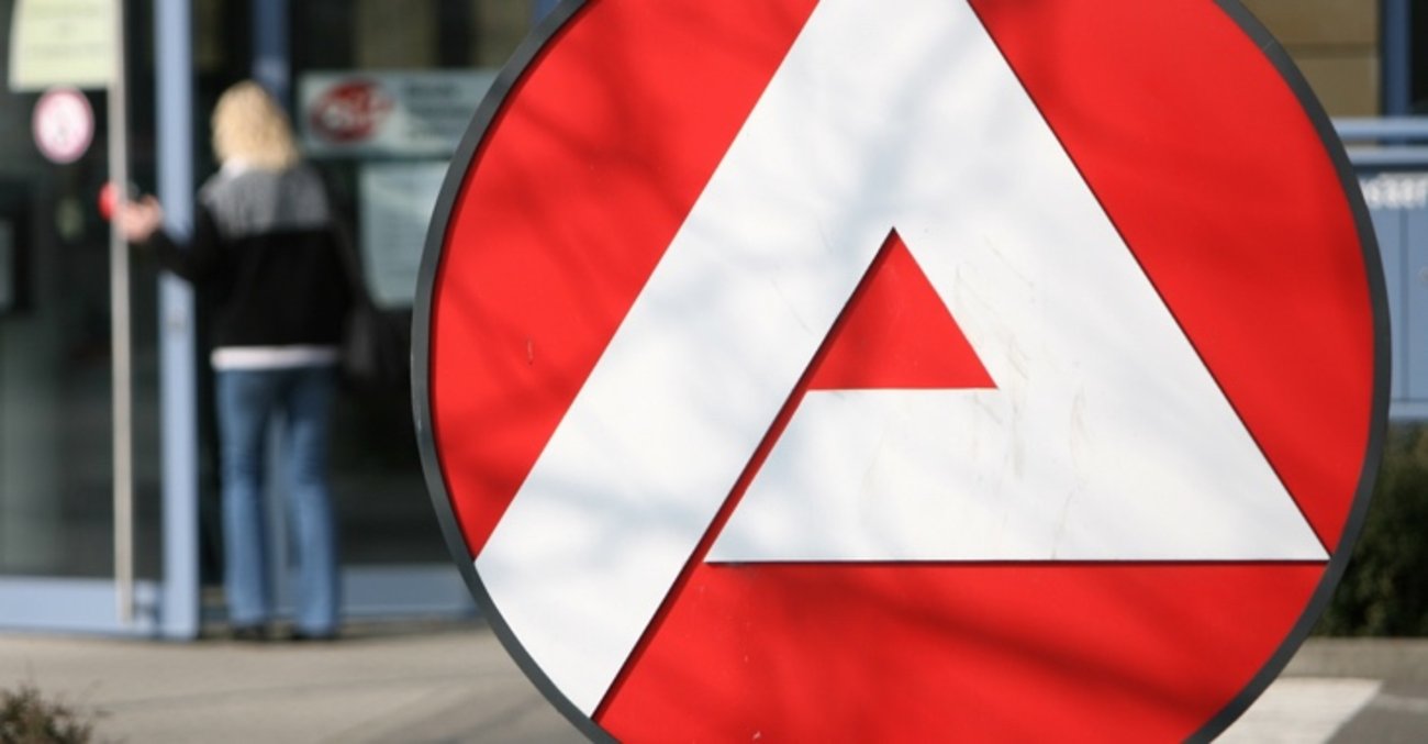 Logo der Agentur für Arbeit, dahinter verschwommen: eine Frau am Eingang eines Jobcenters © ddp images Logo der Agentur für Arbeit, dahinter verschwommen: eine Frau am Eingang eines Jobcenters © ddp images