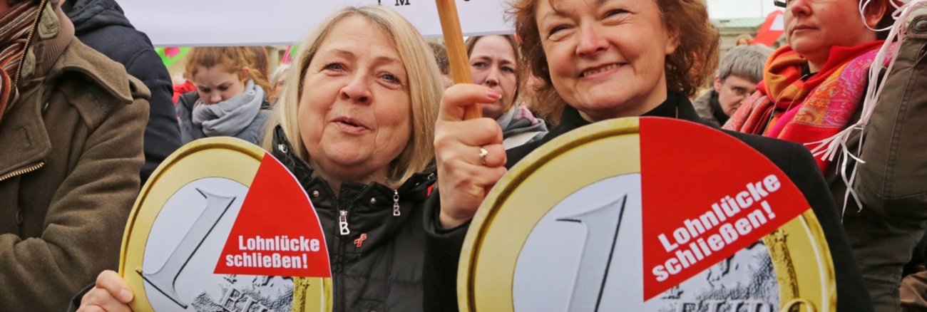Birgit Wöllert und Kerstin Kassner halten am Equal Pay Day Schilder in Form einer Ein-Euro-Münze mit der Aufschrift: Lohnlücke schließen Birgit Wöllert und Kerstin Kassner halten am Equal Pay Day Schilder in Form einer Ein-Euro-Münze mit der Aufschrift: Lohnlücke schließen