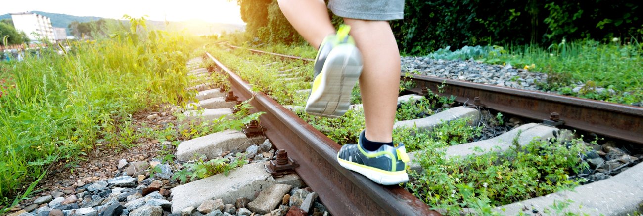 Ein Junge balanciert auf stillgelegten, mit Unkraut bewachsenen Bahngleisen © iStock/baona Ein Junge balanciert auf stillgelegten, mit Unkraut bewachsenen Bahngleisen © iStock/baona