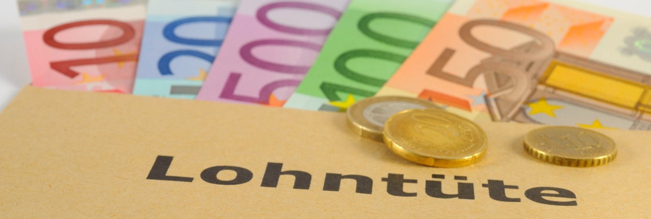 Euro-Münzen auf einem Umschlag mit der Aufschrift Lohntüte, darunter Euro-Scheine © iStock/filmfoto