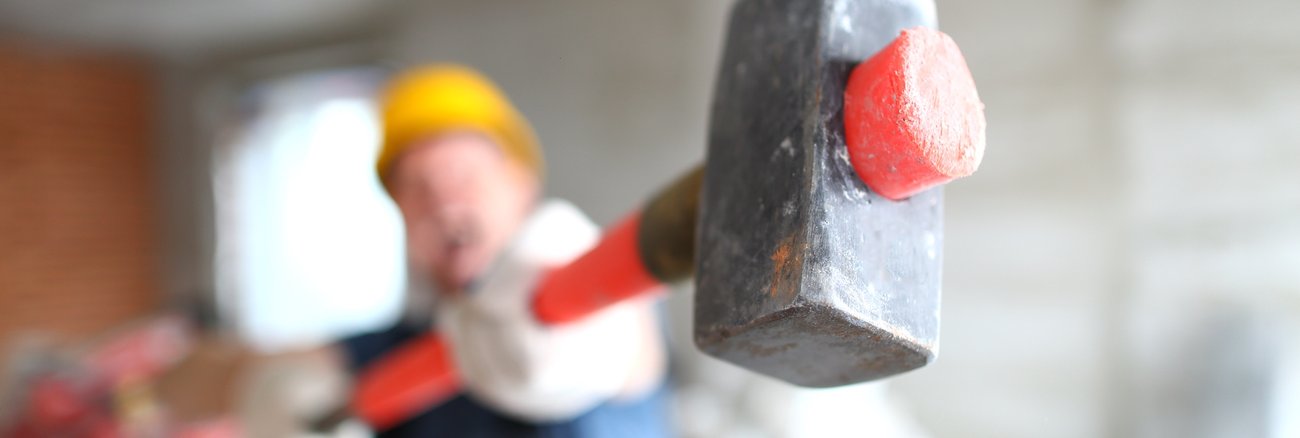 Bauarbeiter mit gelbem Helm hält einen Vorschlaghammer © iStock/Ivan-balvan
