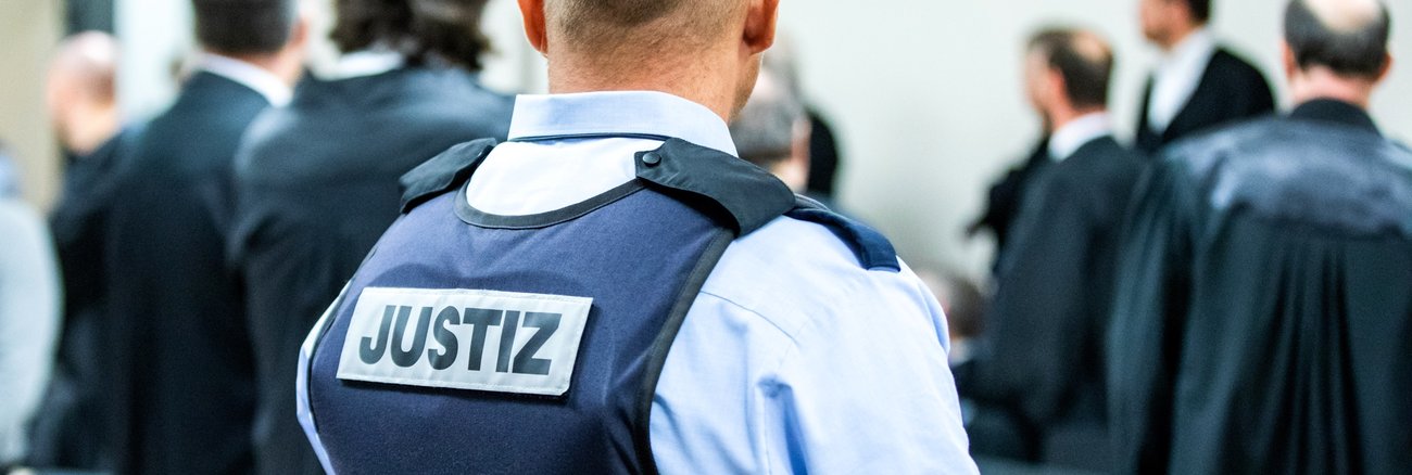 Ein Justizbeamter in einem Gerichtssaal trägt eine Schutzweste mit der Aufschrift Justiz © dpa/Marcel Kusch Ein Justizbeamter in einem Gerichtssaal trägt eine Schutzweste mit der Aufschrift Justiz © dpa/Marcel Kusch