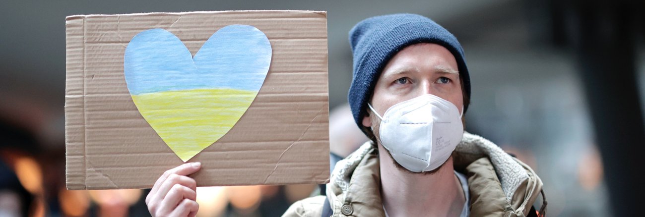 Ein Mann auf dem Berliner Hauptbahnhof hält ein Schild mit einem Herz in den Farben der ukrainischen Flagge. © picture alliance/SZ Photo|Jens Schicke Ein Mann auf dem Berliner Hauptbahnhof hält ein Schild mit einem Herz in den Farben der ukrainischen Flagge. © picture alliance/SZ Photo|Jens Schicke
