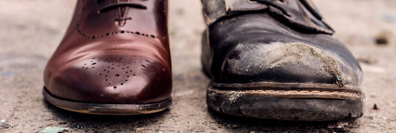 Ein polierter brauner Lederschuh neben einem abgetragenen schwarzen Schuh © iStock/monstArrr_